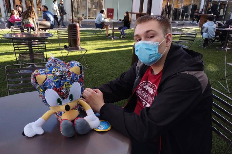 A man wearing a mask sitting next to a stuffed animal.