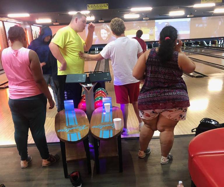 A group of people standing around at the bowling alley.