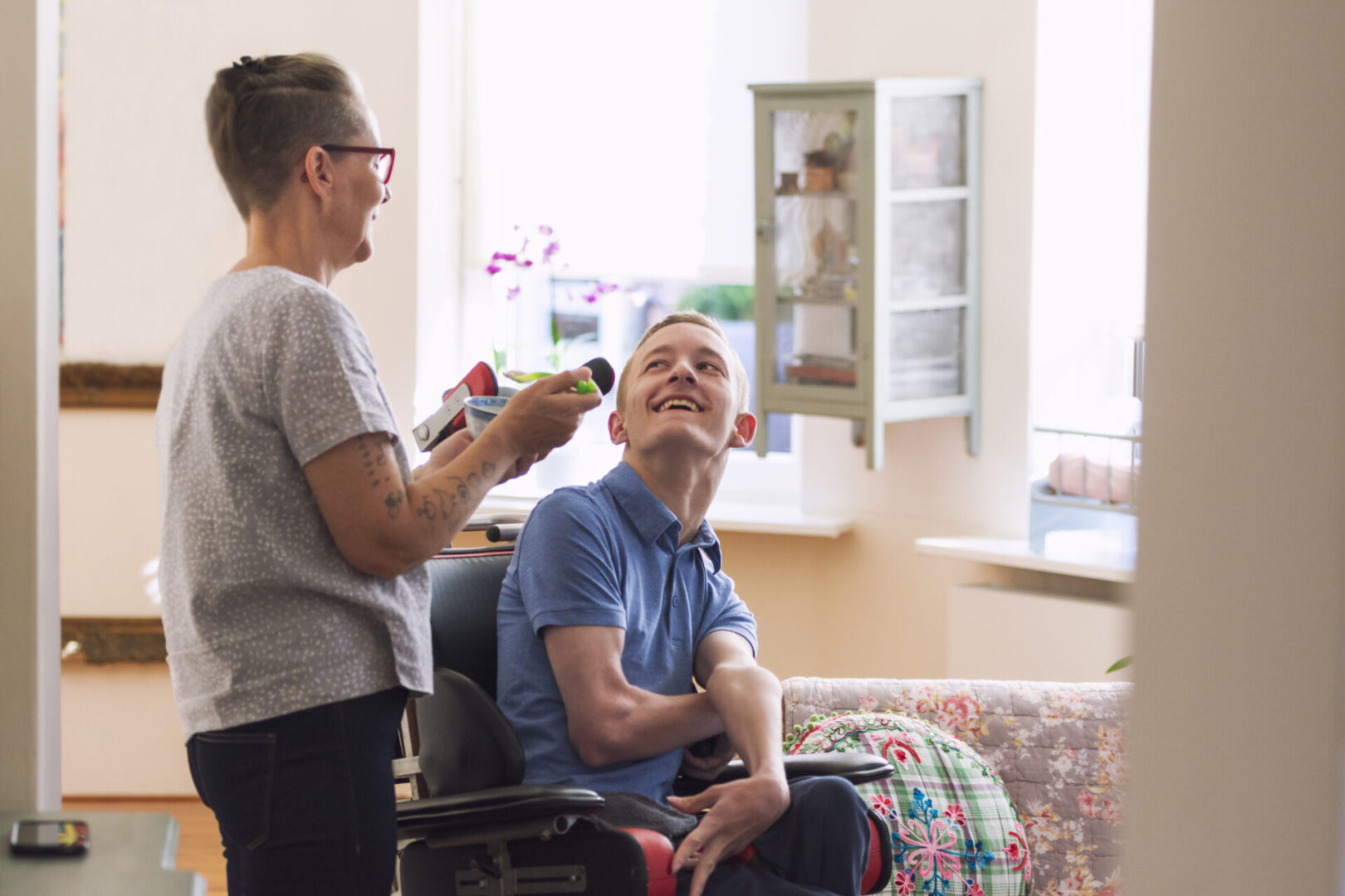 A woman is brushing the hair of a man in a wheelchair.